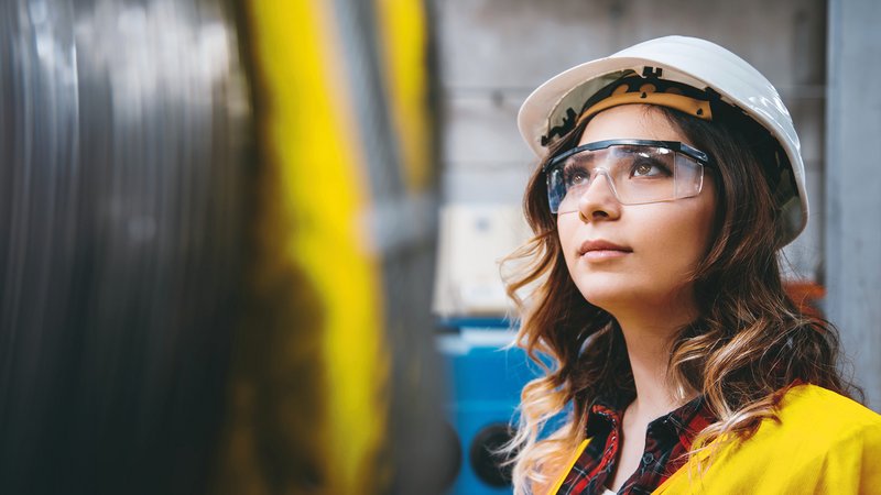 Frau im Lager mit Helm und Schutzbrille, aufschauend nach links oben